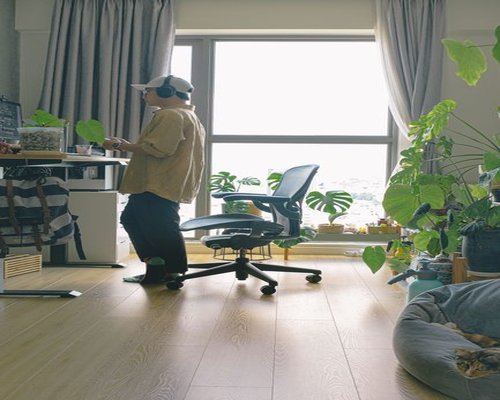 Person standing up from their home office desk looking out a window